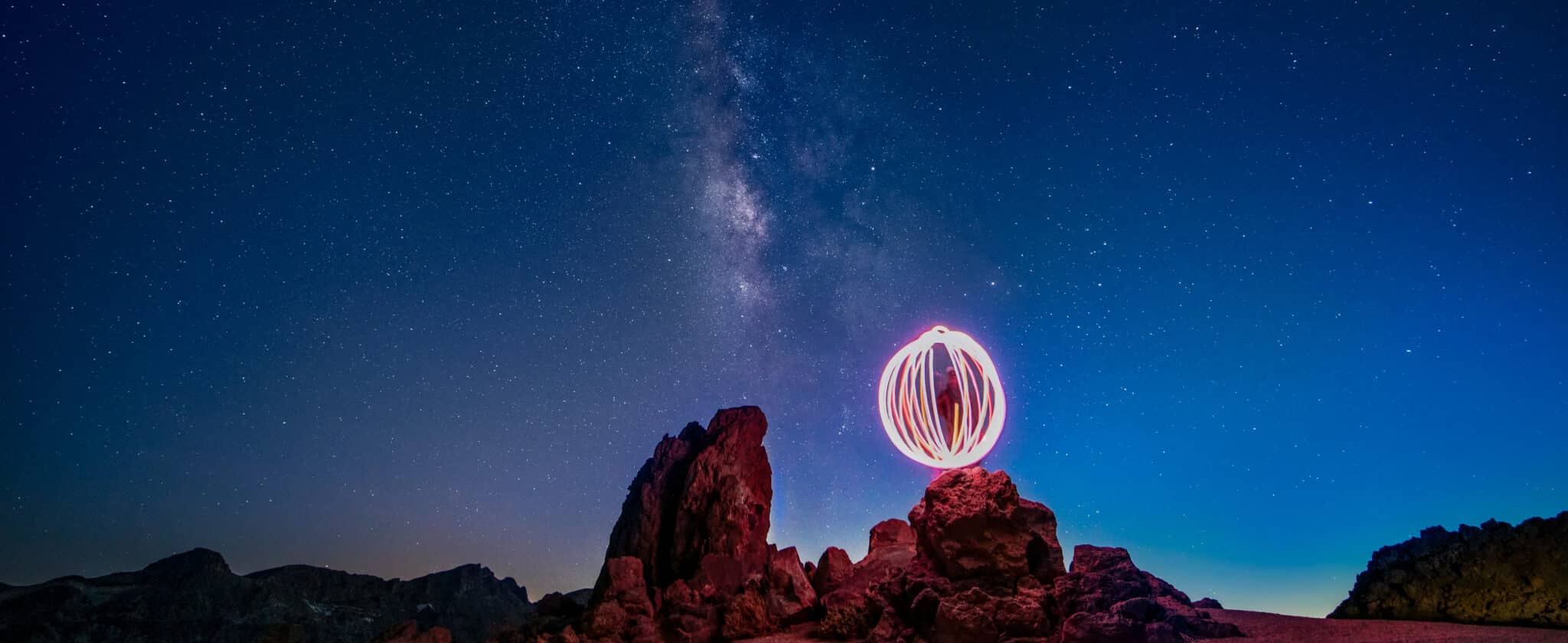 Poi spinner under the Milky Way on desert rocks